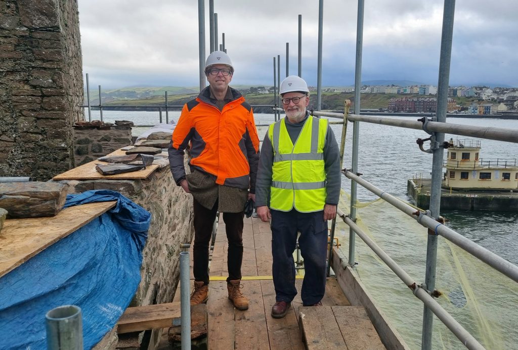 Photograph of MNH Historic Buildings Architect John Paul Walker, pictured with the Very Revd Nigel Godfrey, Dean of Peel Cathedral, pictured at the newly conserved Causeway Wall at Peel Castle, February 2026.